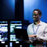Cheerful technician doing checkup in server farm providing vast computing resources and storage. Data center enabling artificial intelligence to process massive datasets for training and inference